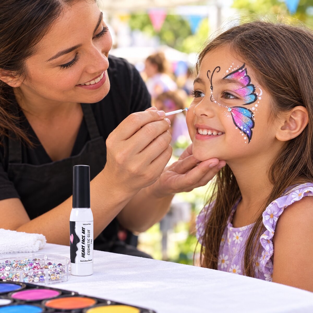 Face painter applying gems and rhinestones to a child butterfly face paint design using Heart Face Art Cosmetic Glue